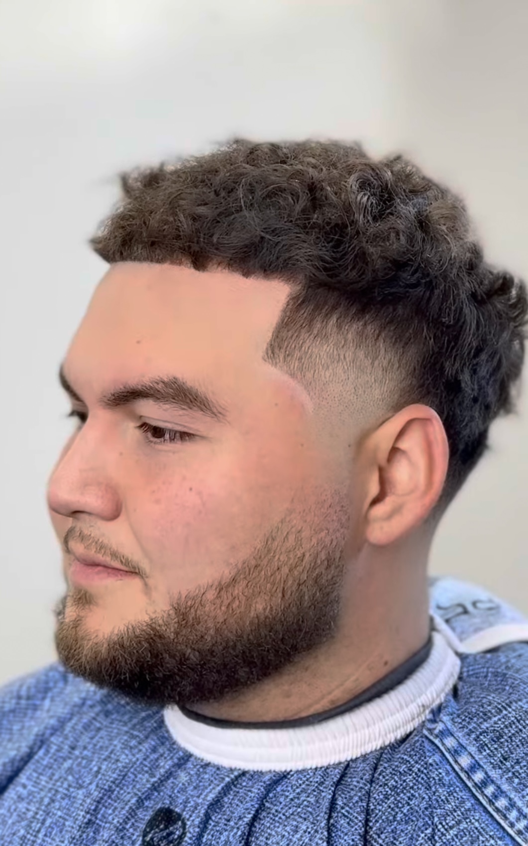 Curly top with low taper fade and beard by Javistylz